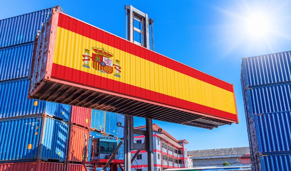 Shipping container being moved featuring Spainsh flag along length of container.